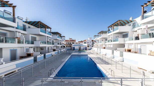A modern hotel with a central swimming pool, multiple balconies, and a clear sky.