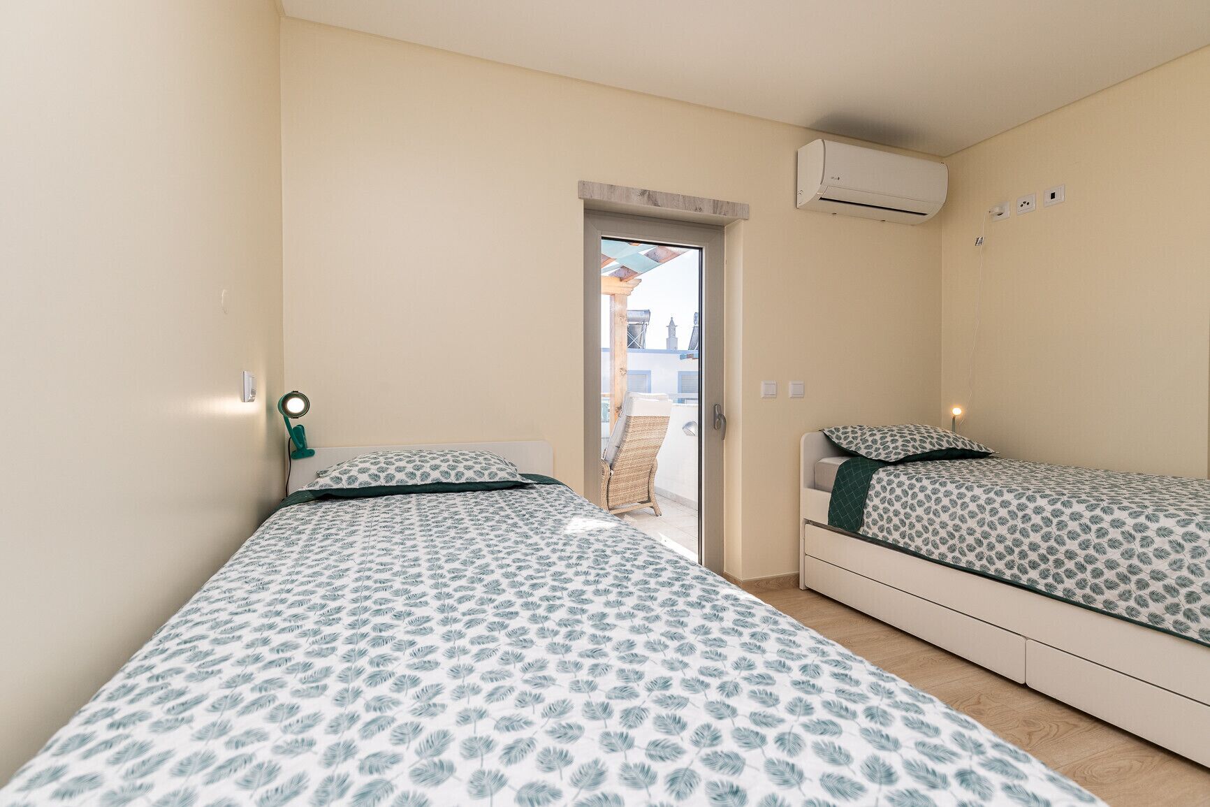 A bedroom with two beds, a window, an air conditioning unit, and a door leading to an outdoor area.