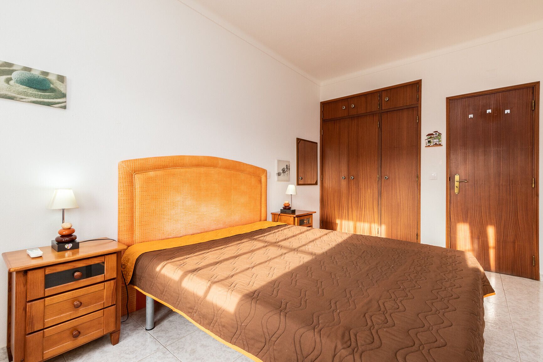 Un dormitorio con cama, mesitas de noche de madera, cómoda y armario.
