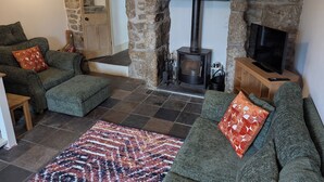 Una sala de estar acogedora con chimenea de piedra, sofás verdes y un televisor.