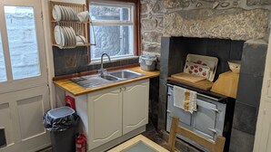 Una cocina con pared de piedra, encimera de madera, pileta y estufa.