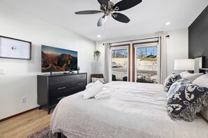 Un dormitorio con cama, ventilador de techo, cómoda, televisión y ventana con vistas al exterior.