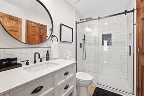 Un baño moderno con lavamanos blanco, grifo negro y cabina de ducha con mampara de vidrio.