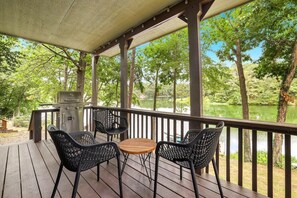 A covered outdoor area with a grill, two chairs, and a table overlooking a lake.