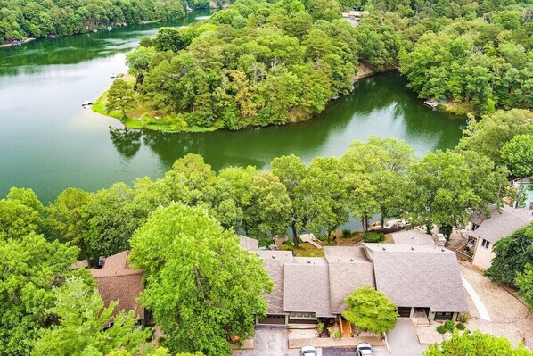 An aerial view of a residential area with houses surrounded by dense greenery and a lake.