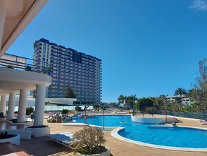 A hotel with a swimming pool, outdoor seating, and a large building in the background. - Luxury Kim Apartment, Ocean View. (Playa Paraíso)
