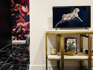 A television on a gold-framed stand with a framed picture of a bird and a candle. - Luxury Kim Apartment, Ocean View. (Playa Paraíso)
