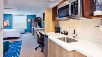 Une chambre d’hôtel moderne équipée d’une kitchenette, d’un lit, d’un bureau et d’une grande fenêtre.