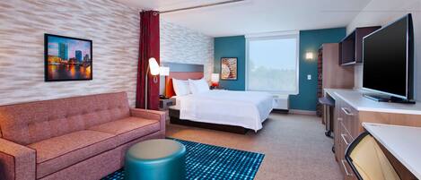 A modern hotel room with a bed, a sofa, a TV, and a desk.
