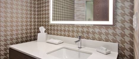 A bathroom with a white sink, a mirror, and patterned wallpaper.
