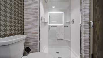 Un baño moderno con ducha de vidrio, inodoro y espejo.