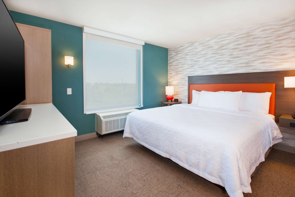 Une chambre d’hôtel équipée d’un lit, d’un bureau, d’une télévision, d’une fenêtre et d’une lampe fixée au mur.