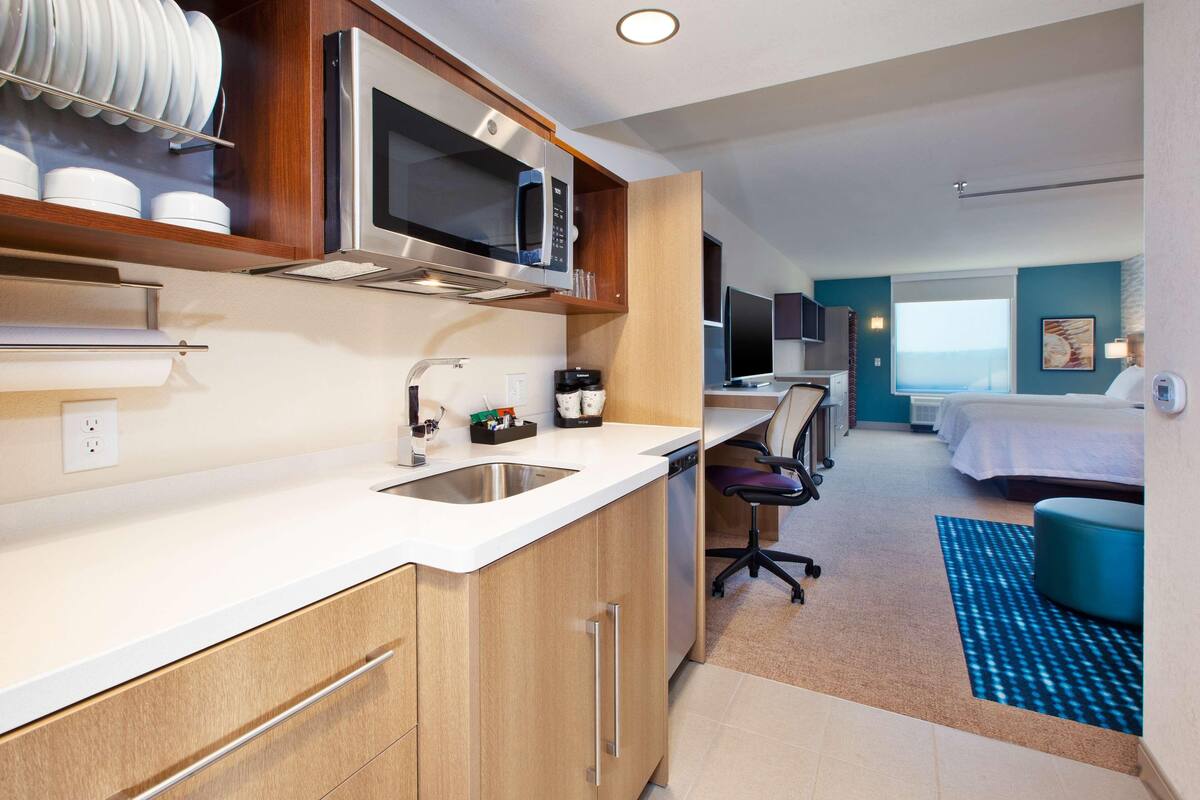 Une chambre d’hôtel moderne équipée d’une kitchenette, d’un lit, d’une télévision et offrant une vue sur l’océan.