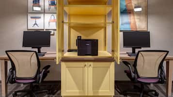 A workspace with two desks, each with a computer monitor, keyboard, and office chair. A central cabinet with a printer is accessible from both desks.