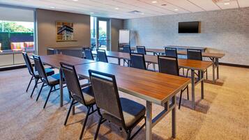 A conference room with a long table, chairs, a whiteboard, and a TV on the wall.
