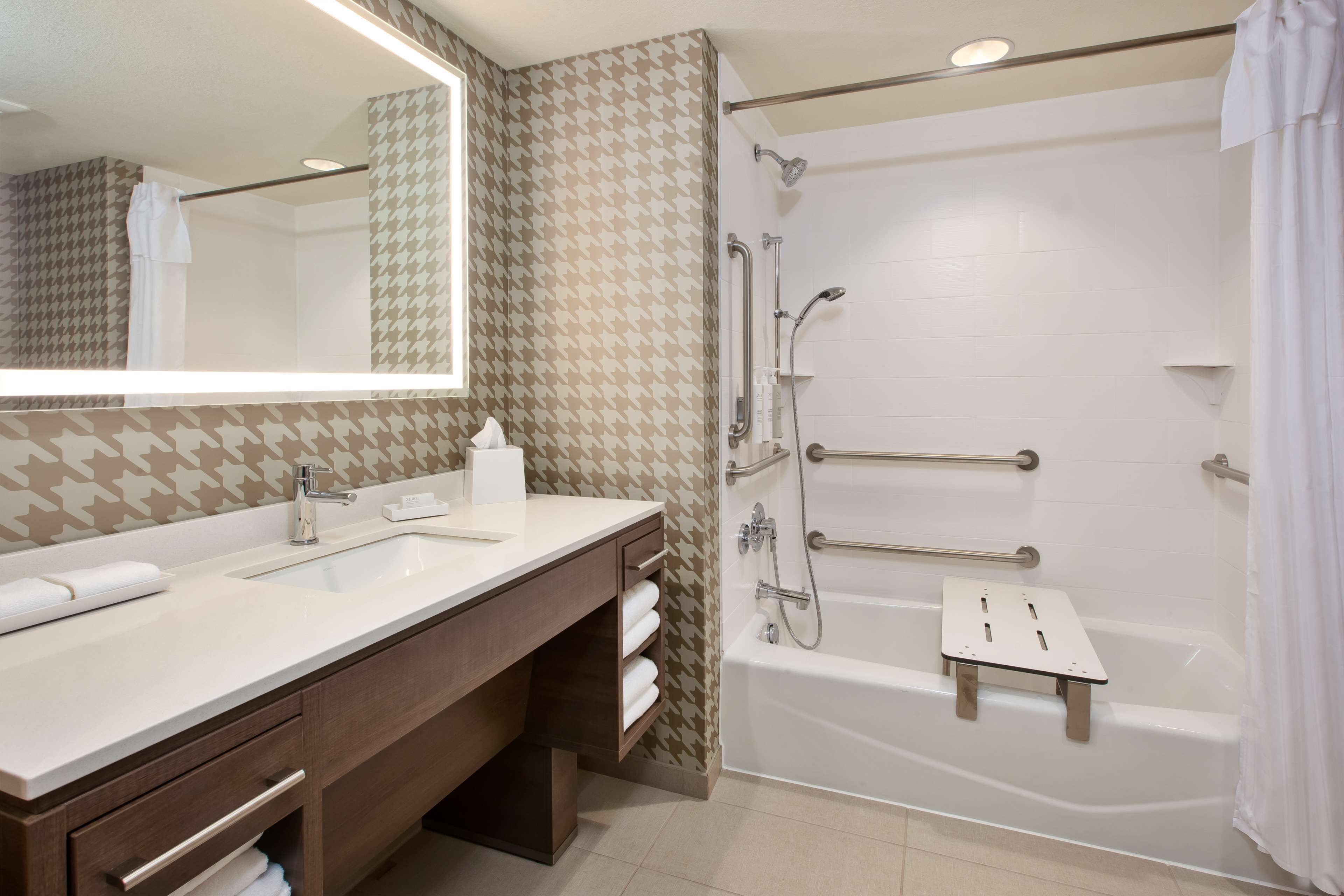 Un baño moderno con lavamanos doble, ducha a ras de suelo con barras de apoyo y bañera blanca.