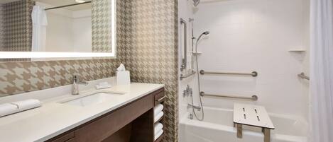 A modern bathroom with a dual sink vanity, a walk-in shower with grab bars, and a white bathtub.