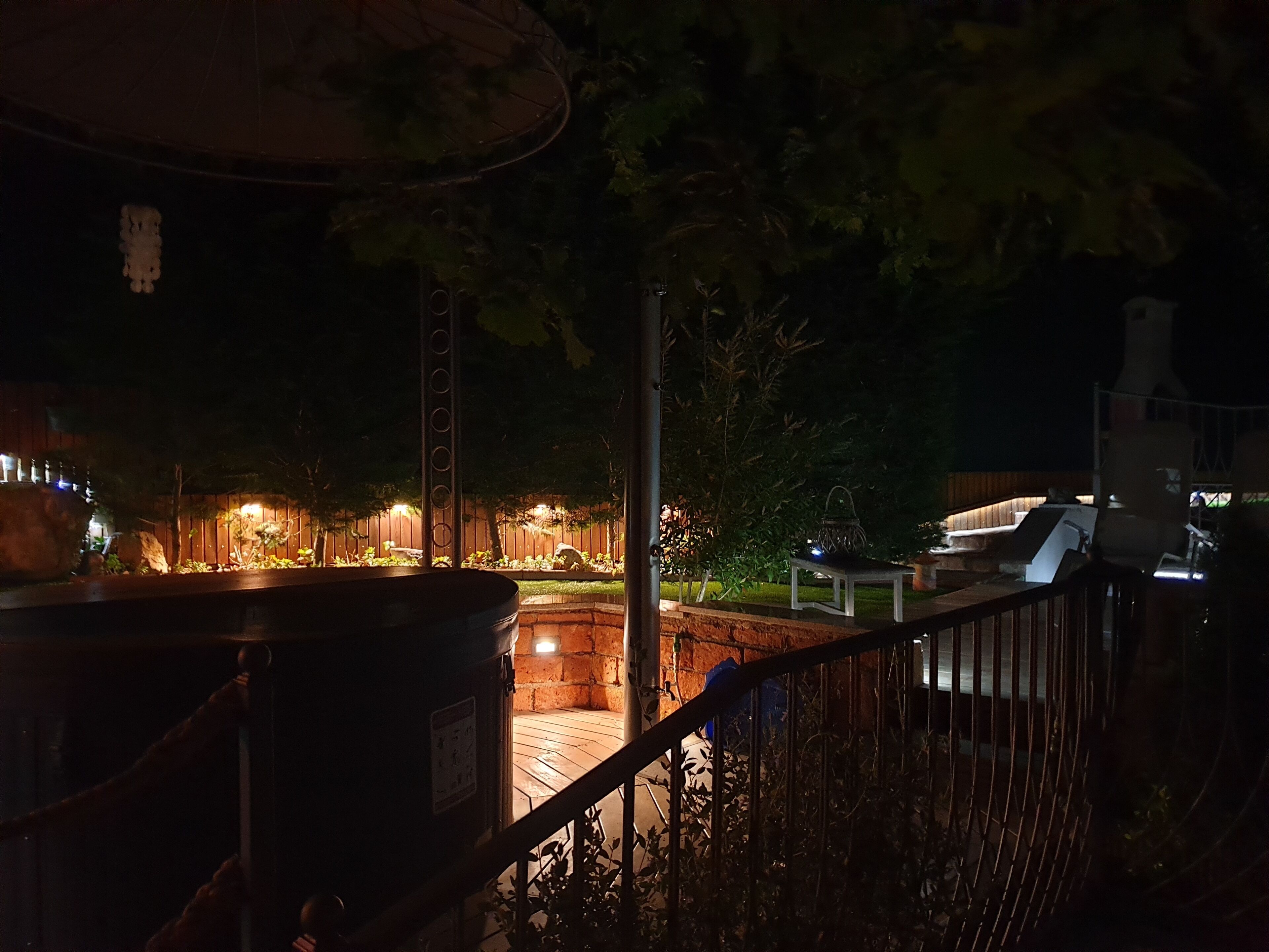 A nighttime view of a courtyard with a brick pathway, a wooden fence, and a metal railing.