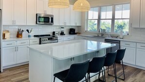 Une cuisine moderne avec des meubles blancs, un grand îlot central doté de tabourets, un four à micro-ondes, une cuisinière et un évier.
