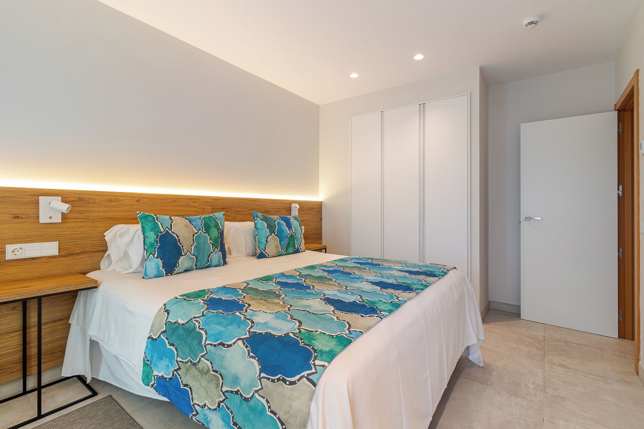 A modern bedroom with a bed, bedside tables, a wooden headboard, and a wardrobe.