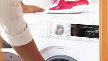 Iemand doet een gekleurd kledingstuk in een wasmachine met een voorlaadklep.