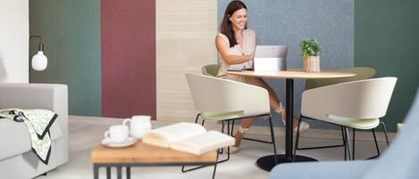 A modern lounge area with a sofa, a small table with a laptop, and a coffee table with a book and a cup.