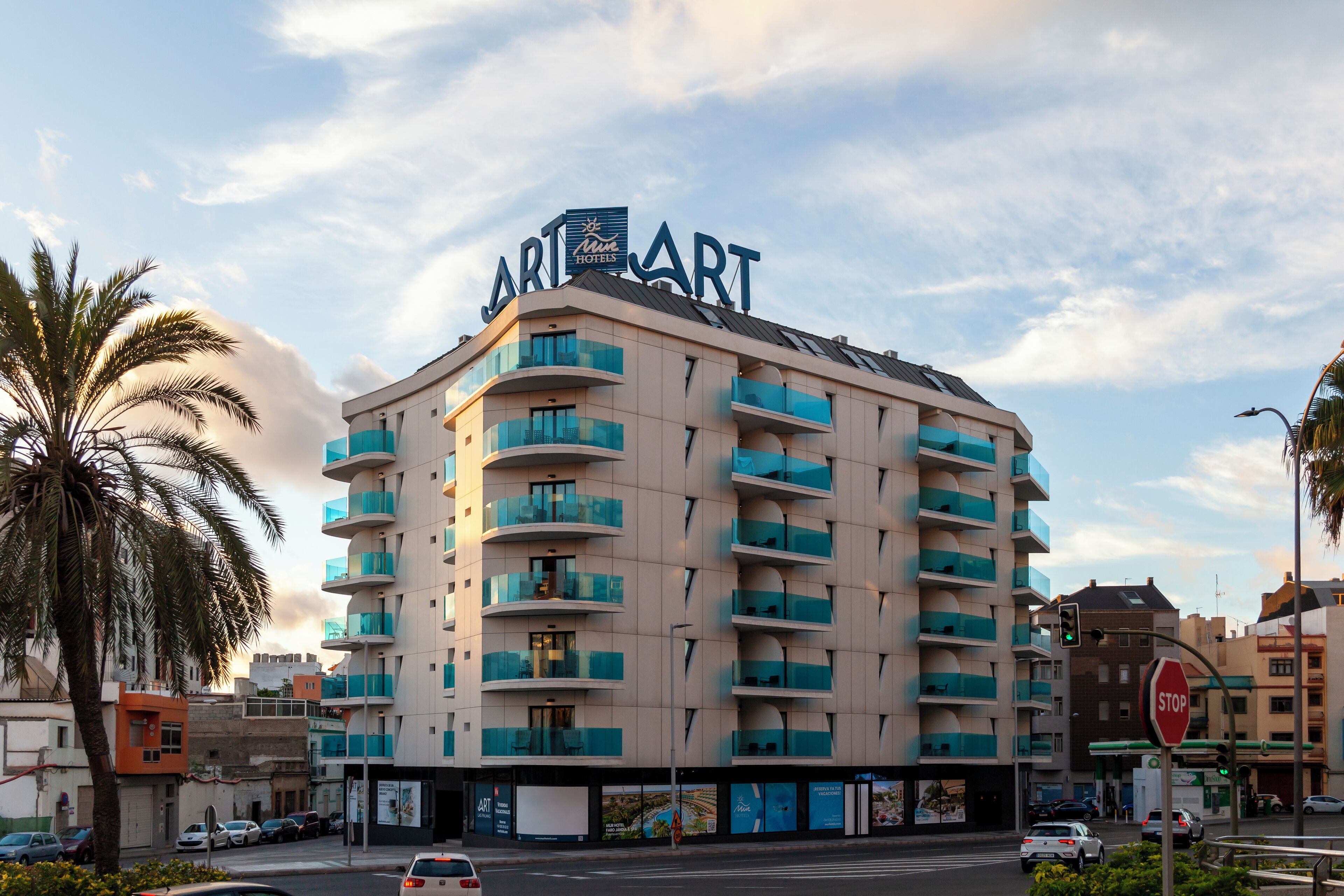A multi-story hotel with balconies, a stop sign, and a palm tree.