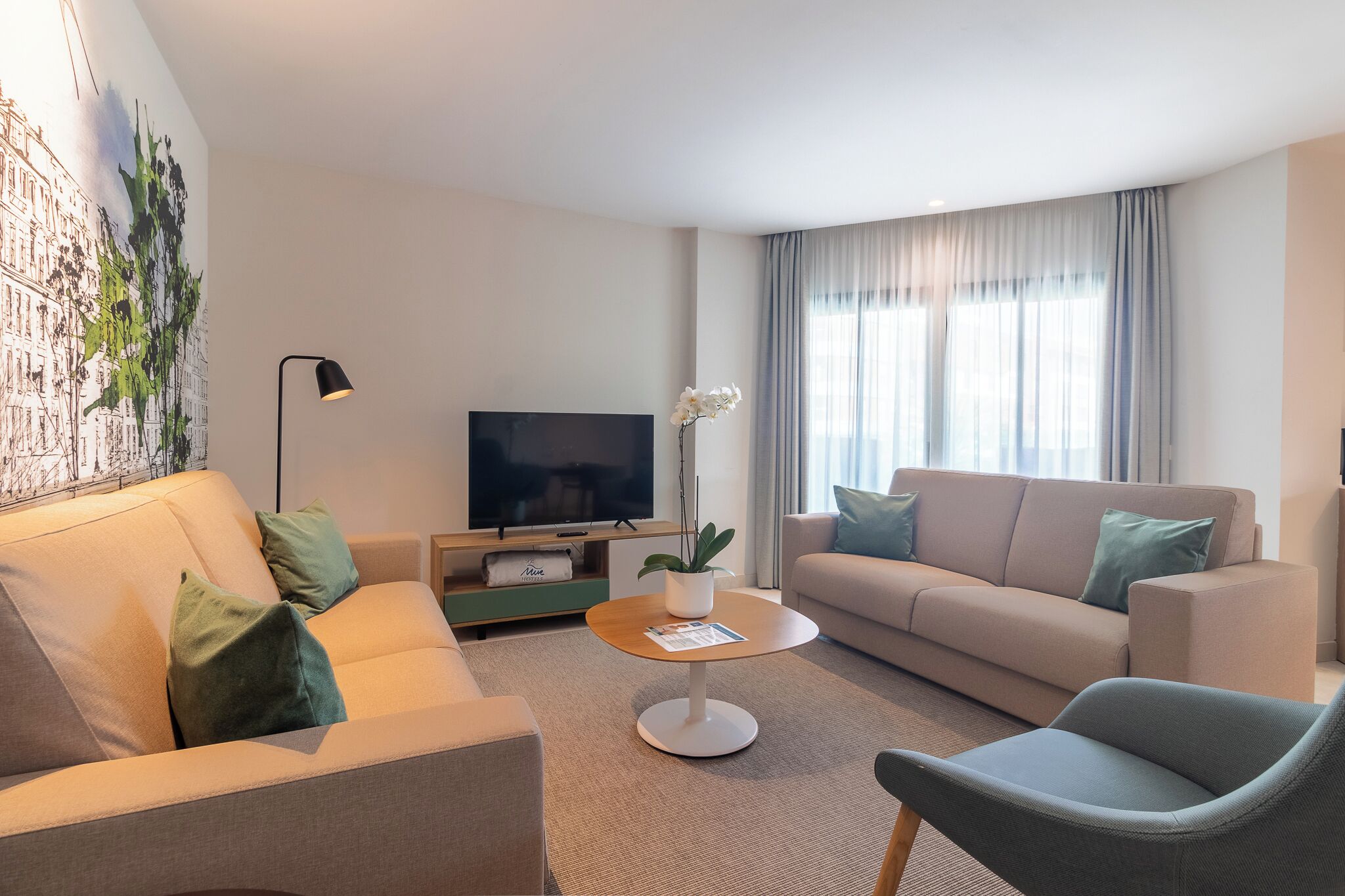 A modern living room with a beige sofa, a grey armchair, a round coffee table, and a flat-screen TV.