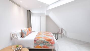 A modern bedroom with a skylight, a bed with colorful bedding, a small table with a glass and apple, and a chair.