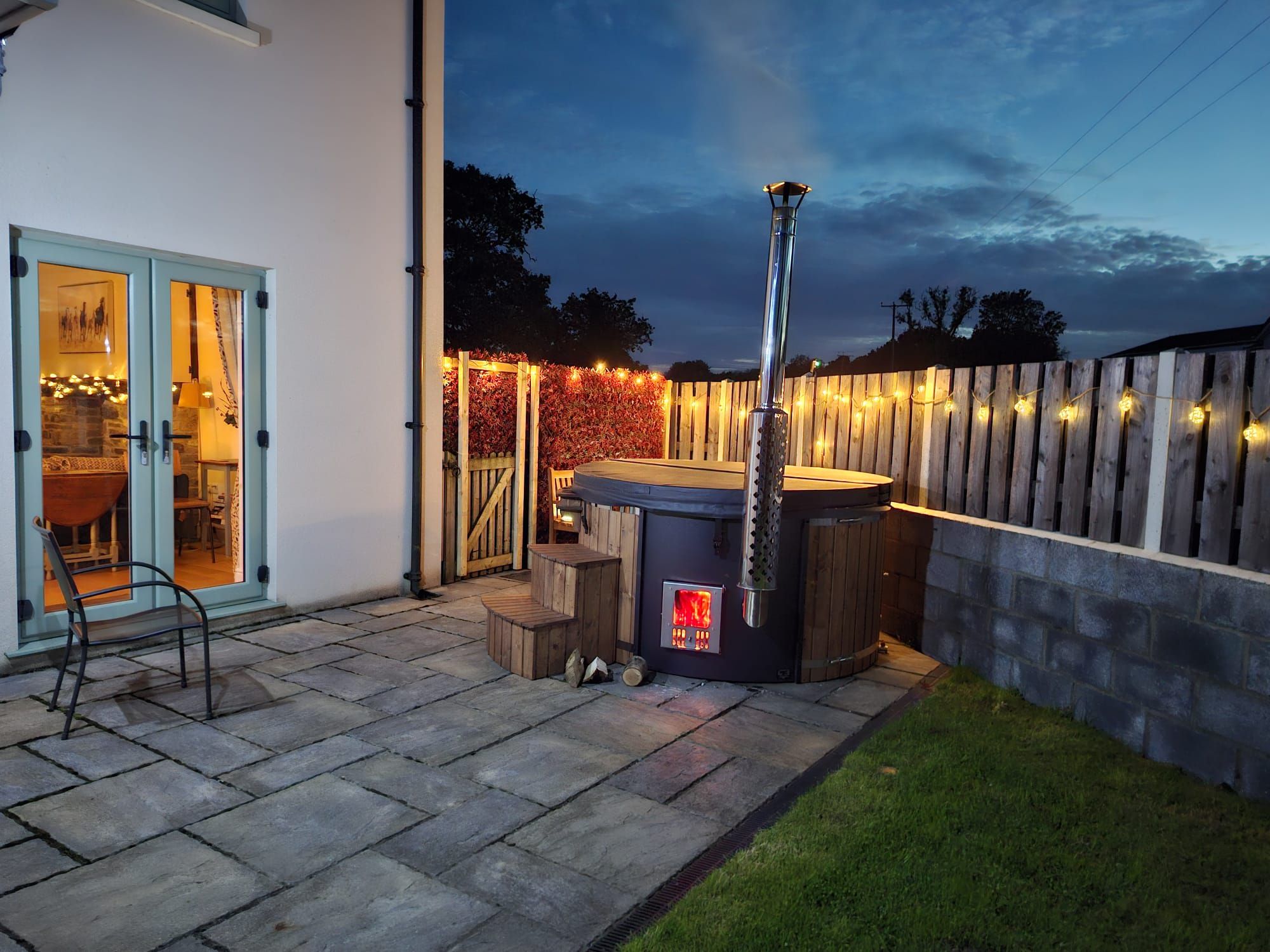 A patio with a hot tub, a wooden fence, and a stone pathway.