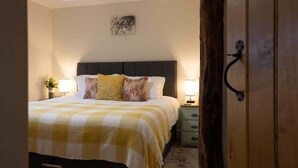 A bedroom with a checkered bedspread, a dark headboard, bedside lamps, a small bedside table with a plant, and a door with a handle. - Brecon Beacons Retreat | 2 Cottages | Hot tub (Myddfai, Llandovery)