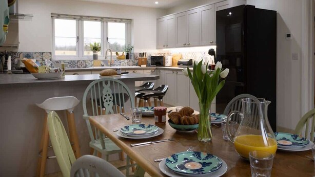 A modern kitchen with white cabinets, a black refrigerator, and a dining table set with plates, a pitcher of orange juice, and a vase of flowers. - Brecon Beacons Retreat | 2 Cottages | Hot tub (Myddfai, Llandovery)