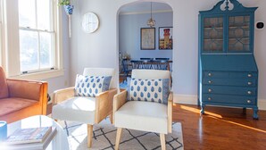 Una sala de estar con un sofá, dos sillones, una mesa de centro, un aparador azul y un reloj en la pared.