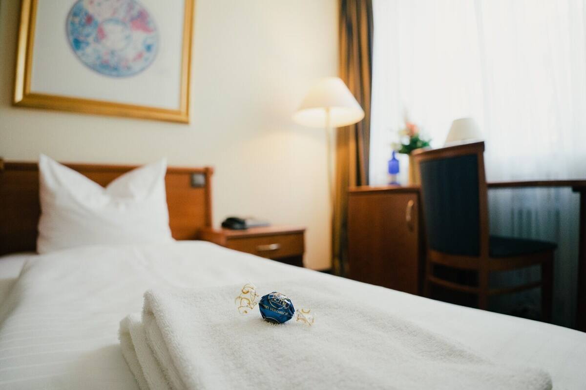 A hotel room with a neatly made bed, a lamp, a chair, and a desk.