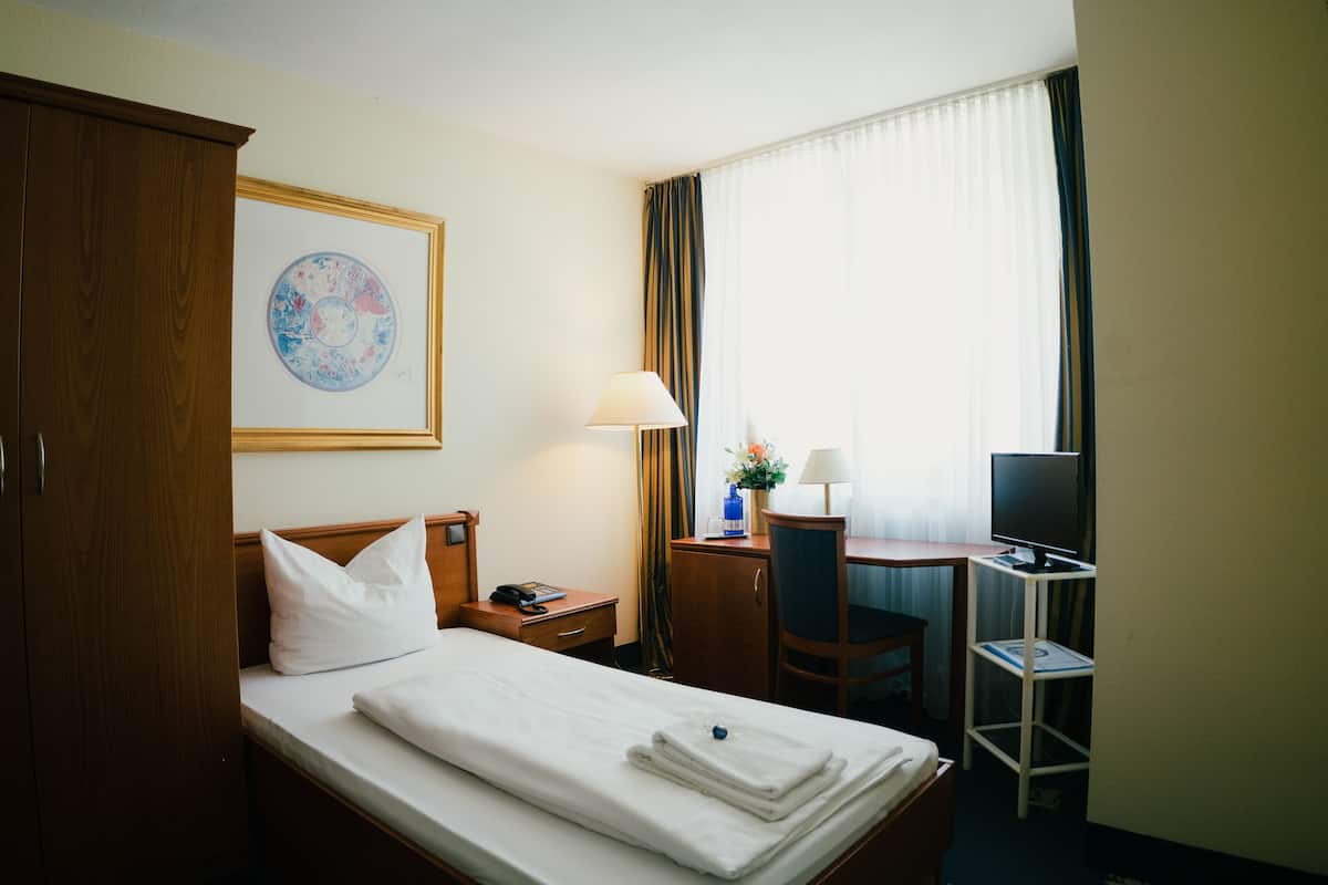 A hotel room with a bed, a desk, a chair, a television, and a framed picture on the wall.