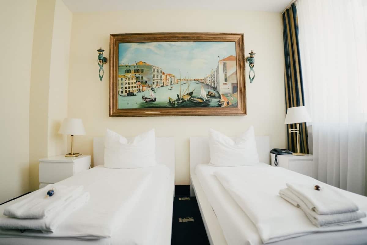 A hotel room with two beds, a painting of a canal scene, a lamp, and a telephone.