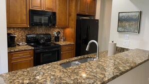 Una cucina con mobili in legno, un forno a microonde nero, un frigorifero in acciaio inossidabile, un piano di lavoro in granito e un lavello in acciaio inossidabile.