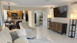 Un soggiorno con un divano, una TV, un mobile e una cucina sullo sfondo.