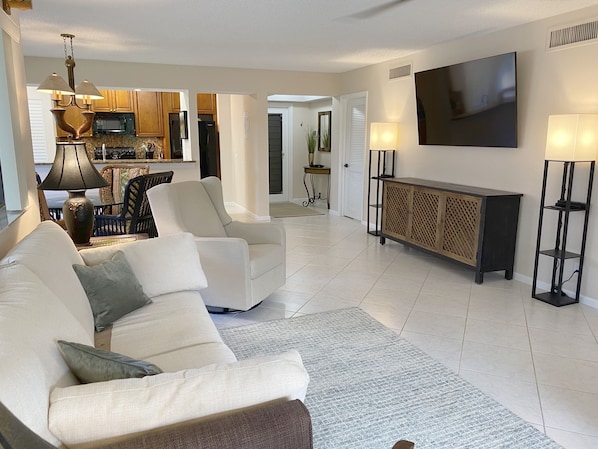 A living room with a sofa, a TV, a cabinet, and a kitchen in the background.