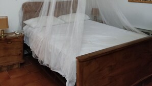 A bedroom with a wooden bed, white bedding, a wooden nightstand, a lamp, and a wall hanging. - Sestino, Sasso di Simone Natural Park (Sestino)