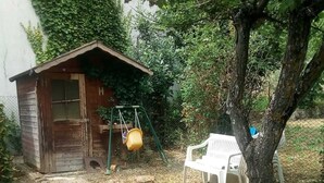 A rustic wooden shed with a door and windows, a swing set with a yellow bucket, and a white plastic chair under a tree. - Sestino, Sasso di Simone Natural Park (Sestino)