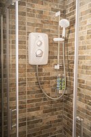 A shower with a control panel, a handheld showerhead, and a bottle of shampoo on a shelf.