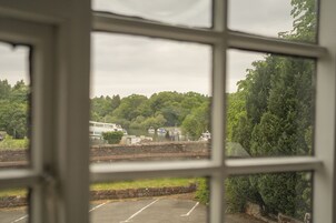 Vista a través de una ventana que muestra un estacionamiento, una carretera, árboles y un edificio al fondo.