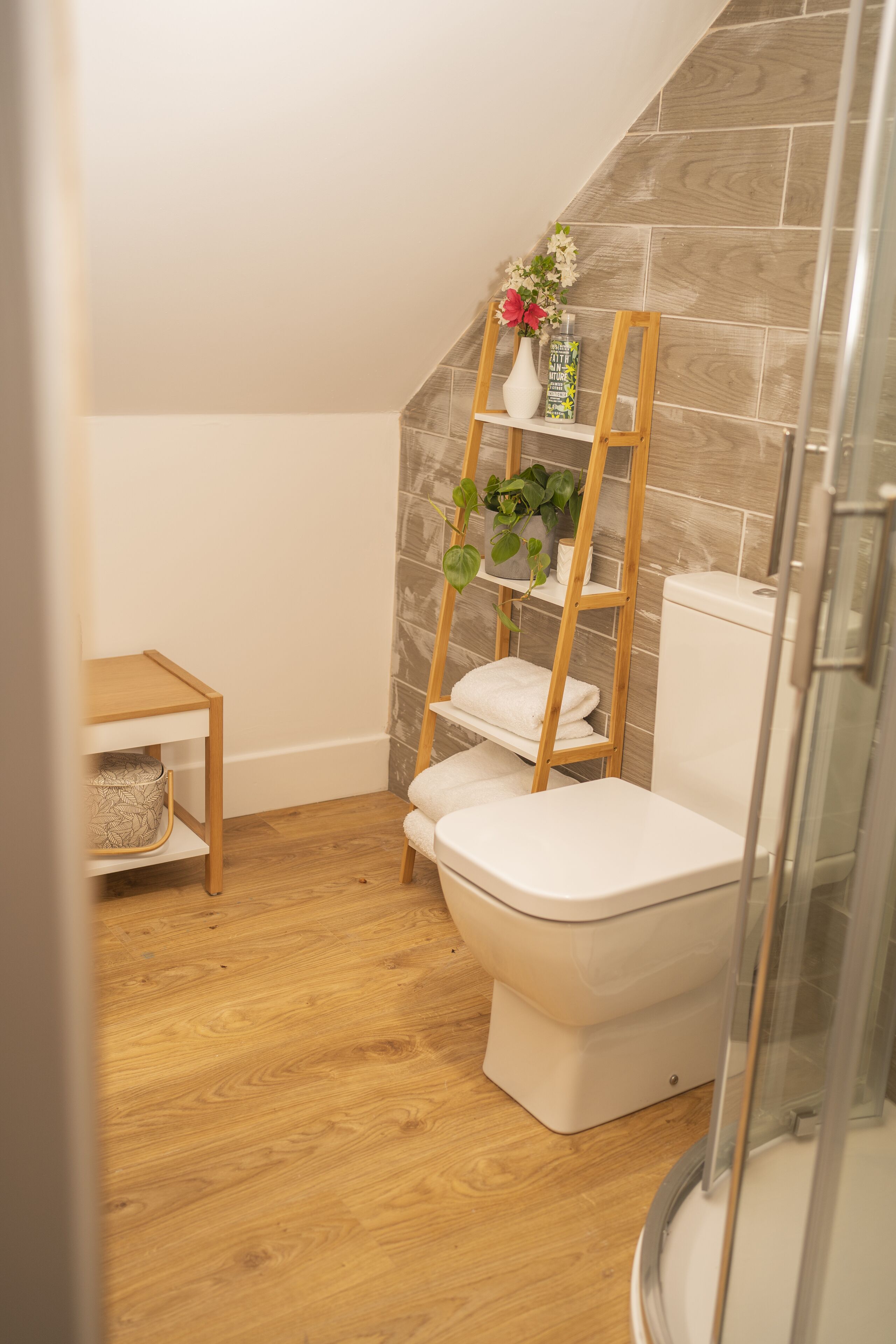 Ein Badezimmer mit Toilette, Holzboden, Ablagefläche mit Pflanze und Duschbereich.