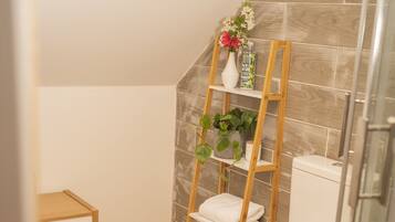 Ein Badezimmer mit Toilette, Holzboden, Ablagefläche mit Pflanze und Duschbereich.
