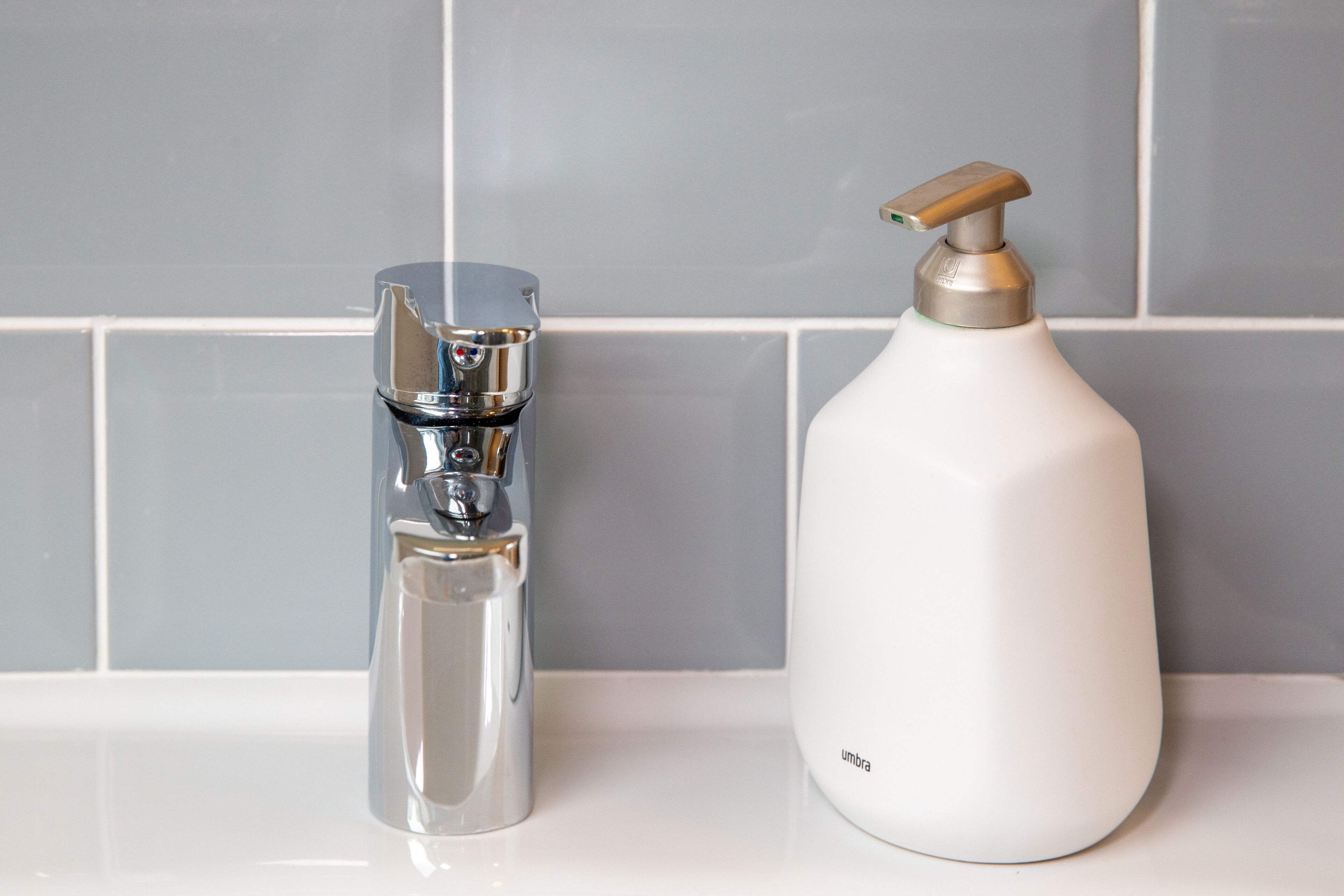 A bathroom with a chrome faucet and a white bottle with a pump dispenser.