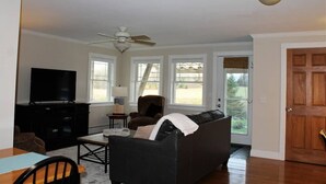 A living room with a black leather couch, a wooden coffee table, a TV on a black stand, and a ceiling fan. - Modern Condo #1! (Ellsworth)