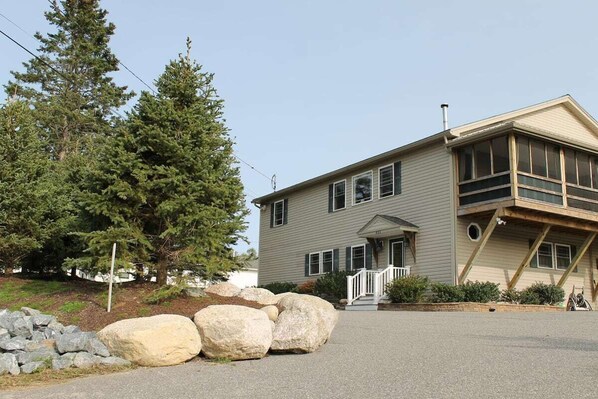 A two-story house with a front porch, large rocks, and a pine tree. - Modern Condo #1! (Ellsworth)