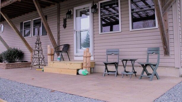 A covered porch with wooden chairs and a table, a wooden ladder, and a window with a view of the sky. - Modern Condo #1! (Ellsworth)