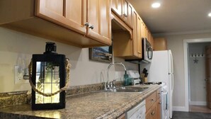 A kitchen with wooden cabinets, a granite countertop, a coffee maker, a sink, a stove, and a refrigerator. - Modern Condo #1! (Ellsworth)